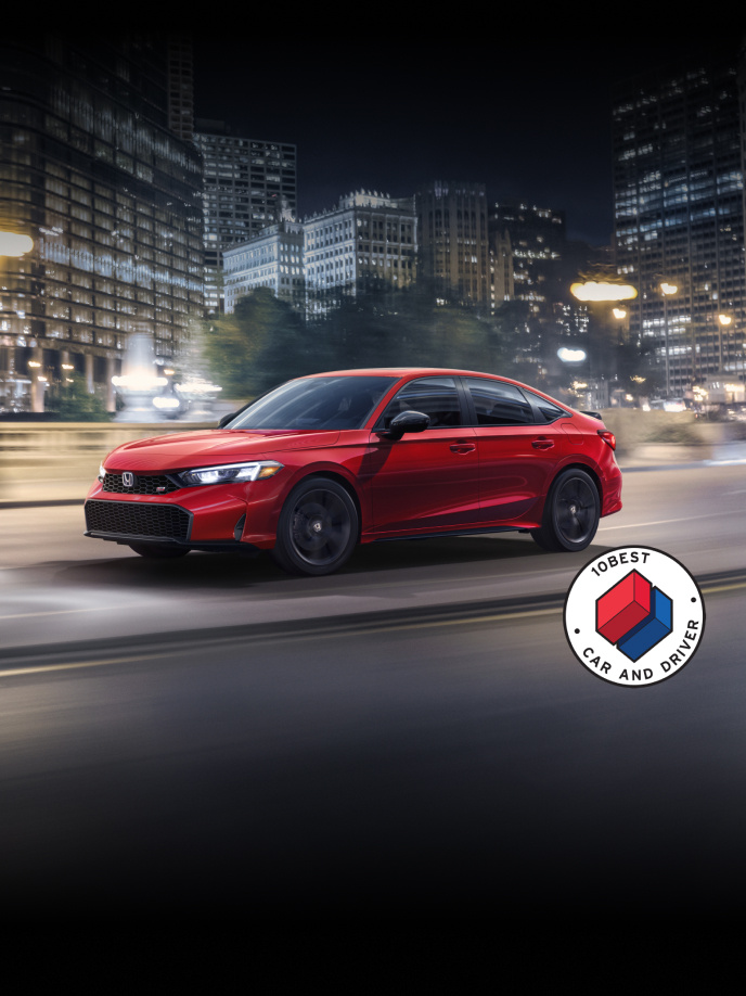 2026 Honda Civic Si Sedan in Rallye Red front 3/4 driving in a city at night with overlapping Car and Driver 10Best logo (Sporty Compact Sedan).
