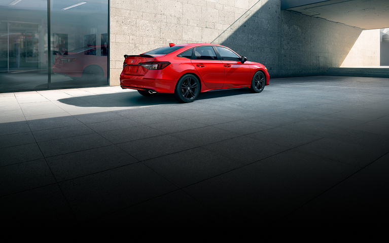 2026 Honda Civic Si Sedan in Rallye Red rear on a tiled floor near a concrete wall and glass reflection (Sporty Compact Sedan).