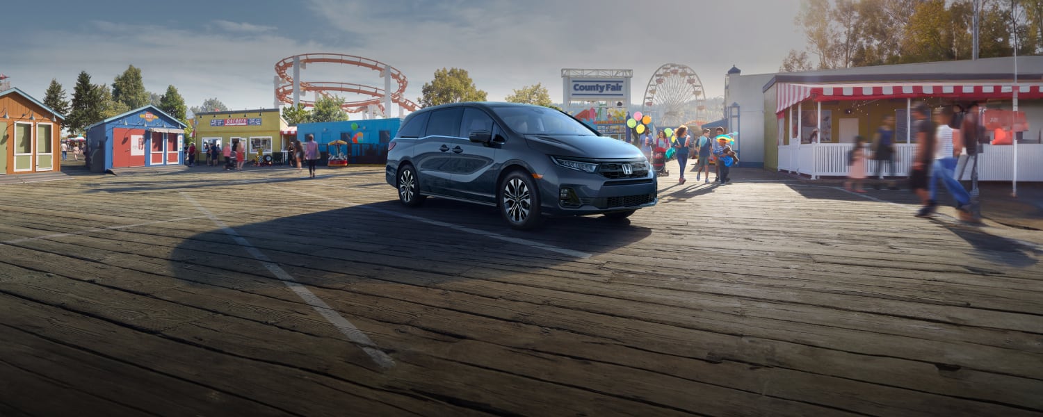 2025 Honda Odyssey Elite shown in Smoke Blue Pearl on a wooden pier of an amusement park.