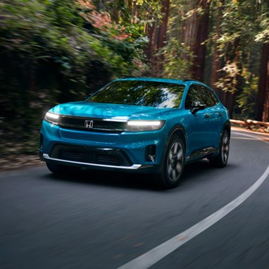 2026 Honda Prologue Elite in North Shore Pearl, driving through redwoods, taking a curved turn on a paved road, with light peeking through the trees in the background.