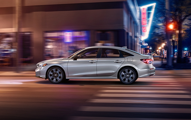 2026 Honda Civic Sedan Sport Touring Hybrid in Solar Silver Metallic side profile driving on a city street (Compact Sedan)