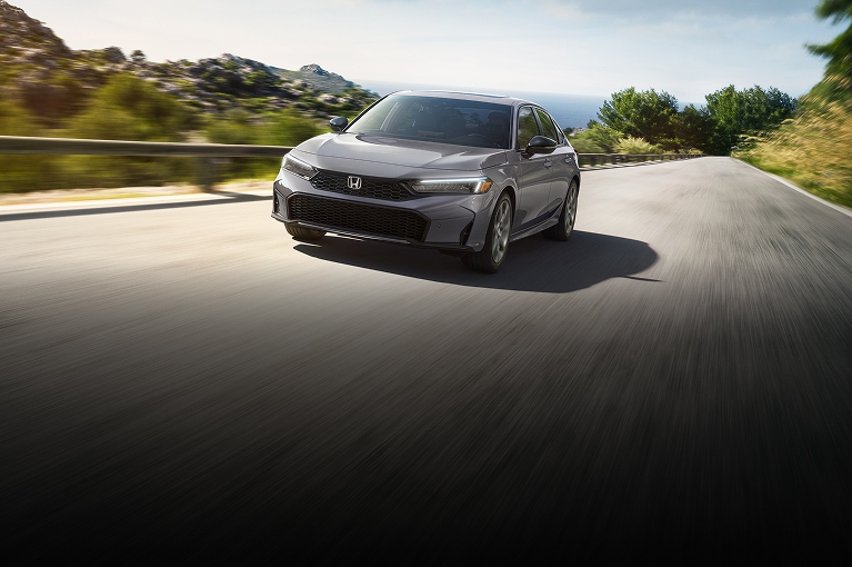 2026 Honda Civic Sedan Sport Touring Hybrid in Urban Gray Pearl front three-quarter view driving on a road (Compact Sedan)