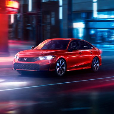 2026 Honda Civic Sedan Sport Touring Hybrid in Rallye Red front three-quarter view driving through a city (Compact Sedan)
