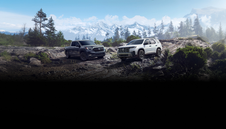 2026 Pilot in Platinum White Pearl next to a 2026 Ridgeline with HPD package in Crystal Black Pearl, parked in an outdoor terrain surrounded by trees.